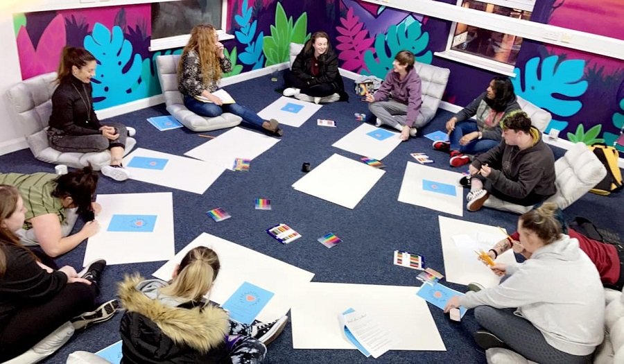 Group work – (Credit: Northern Ireland Youth Forum) Young people sit in a circle on the floor doing group art work.