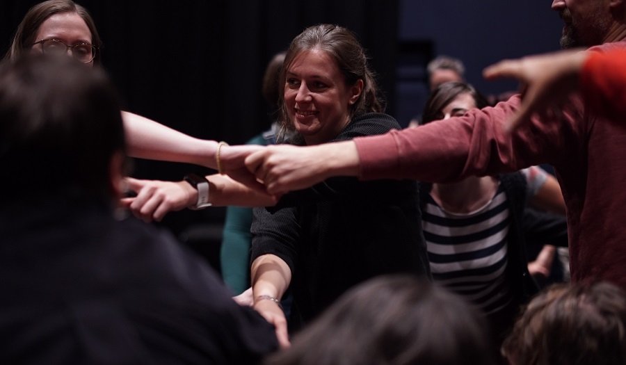 Drama workshop – (Credit: Odd Arts) Young women playing a drama game by holding each others arms in a human 'knot'. They are laughing and smiling.
