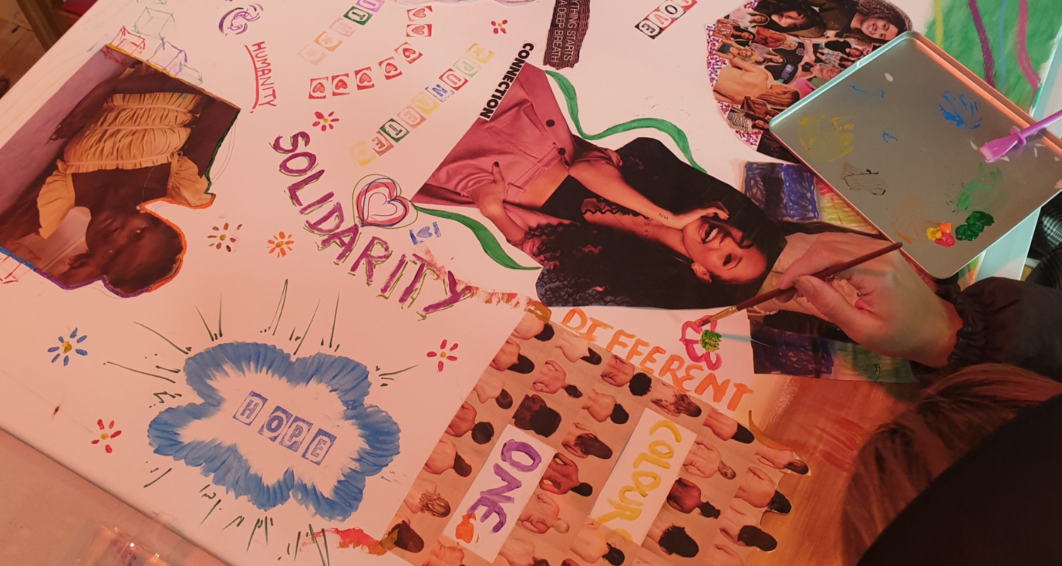 A large poster is being decorated with images of women, patterns, writings about solidarity and confidence and you see the hand of a young women drawing.