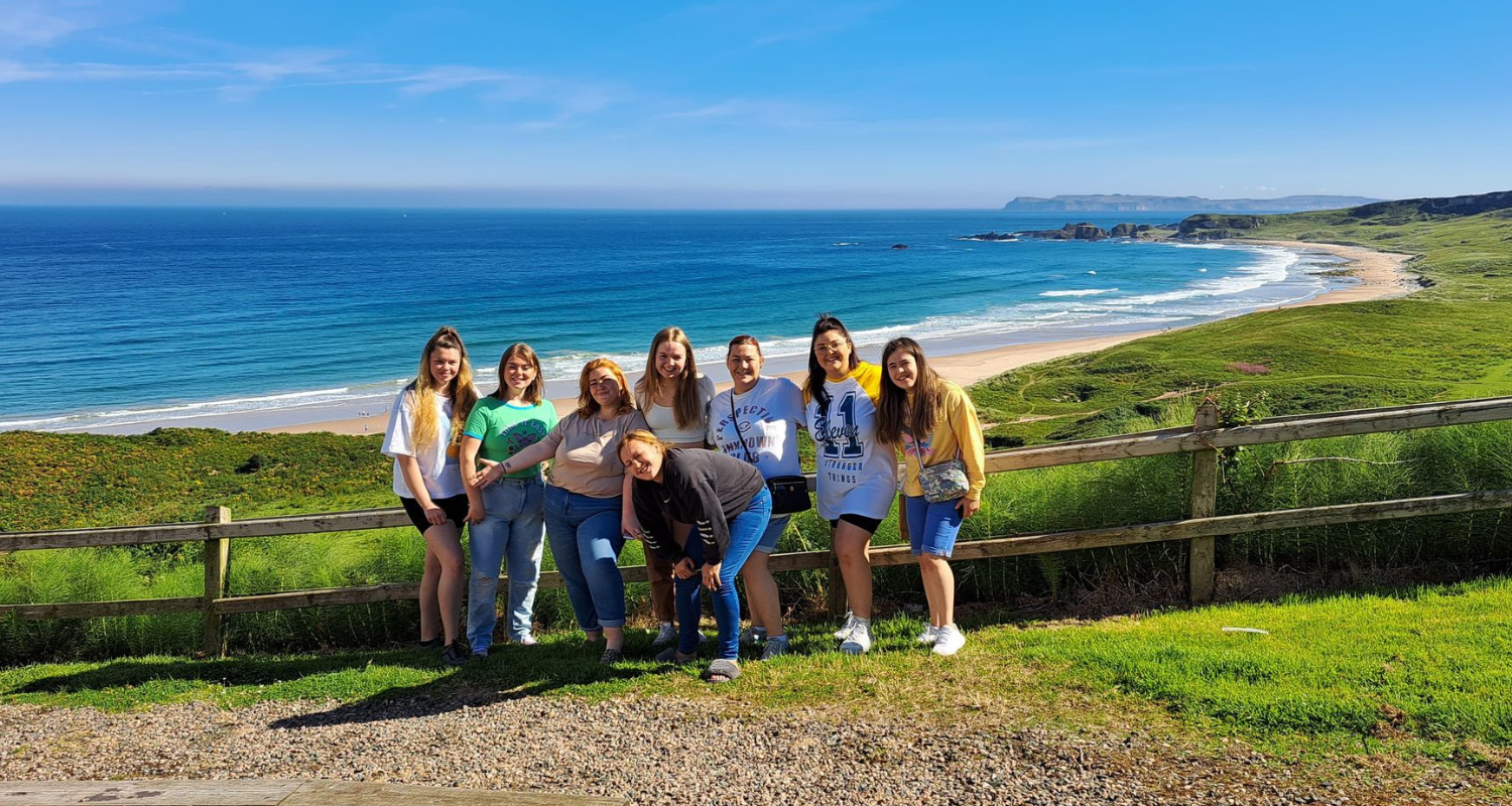 A group of young girls pose for a picture, on a glorious day with a field and beach in the background.