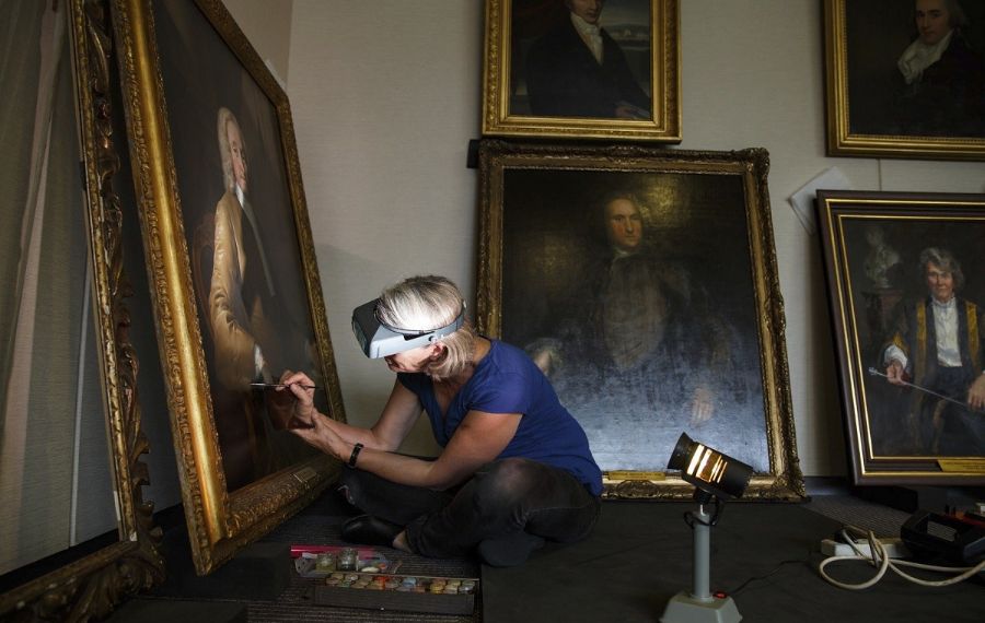 Women with special eye wear is restoring an old portrait using a paintbrush.